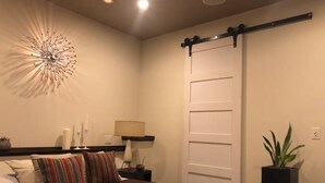 A bedroom with a bed, a nightstand, a lamp, a wall decoration, a sliding door, and a potted plant. - Beautiful Cottage, hot tub, in great neighborhood (San Francisco)