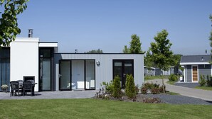 Une maison moderne à deux étages, dotée d’un toit plat, de grandes fenêtres et d’un petit patio aménagé avec du mobilier d’extérieur.