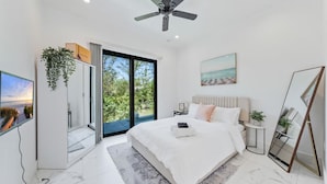 A modern bedroom with a large bed, a ceiling fan, a TV, and a sliding glass door leading to a balcony. - 5bdr/5.5ba Modern Oasis with outdoor Gym, Cold Plunge, Heated Pool & Jacuzzi (Naples)