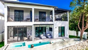 A modern two-story house with a glass-enclosed balcony, a swimming pool, and a well-maintained garden. - 5bdr/5.5ba Modern Oasis with outdoor Gym, Cold Plunge, Heated Pool & Jacuzzi (Naples)