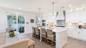 Une cuisine moderne avec des meubles blancs, un îlot central doté de tabourets et un coin repas avec une table et des chaises.
