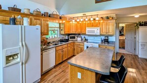 A spacious kitchen with wooden cabinets, a central island with bar stools, and a large window providing natural light. - Charming and Cozy River House (Murphy)