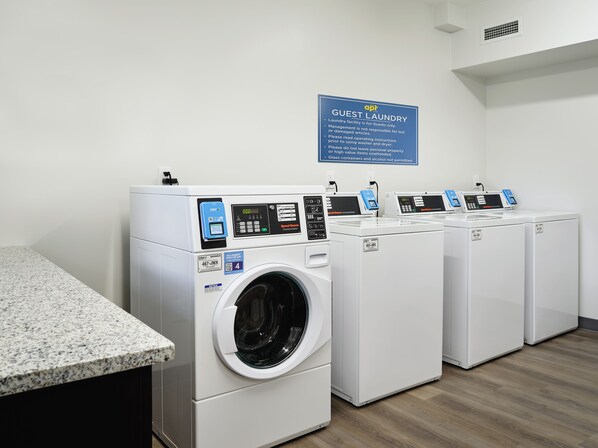 A laundry facility with four front-loading washing machines, a granite countertop, and a sign indicating it's for guests only. - stayAPT Suites Atlanta-Lithia Springs (Lithia Springs)