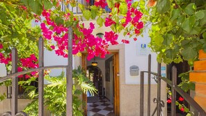 Ein Hotel mit Eingangsbereich, einem Schachbrettmuster-Boden, einem Metallgitter und leuchtend blühendem Bougainvillea.