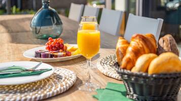 A breakfast setting with a glass of orange juice, croissants, and a plate of fruit.