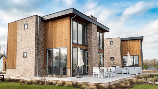 A modern two-story house with large glass windows, a wooden exterior, and a patio with outdoor furniture. - Luxury Villa With Dishwasher (Kerkdriel)