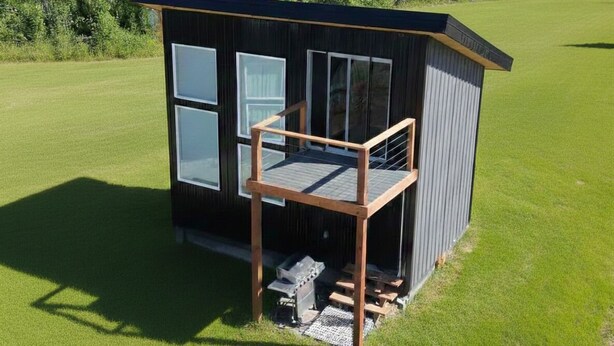 Eine kleine, eingeschossige Hütte mit Balkon, umgeben von einer Wiese und dichtem Wald.