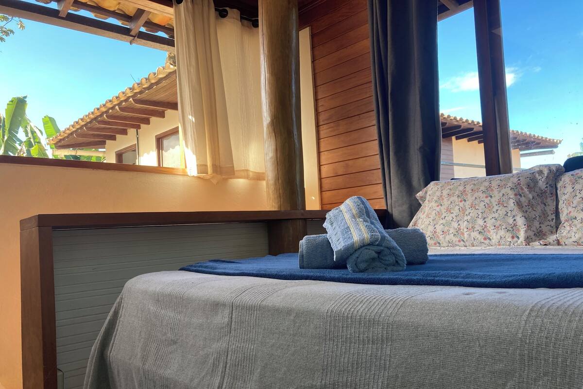 A bed with a grey bedspread, a folded towel, and floral-patterned pillows.