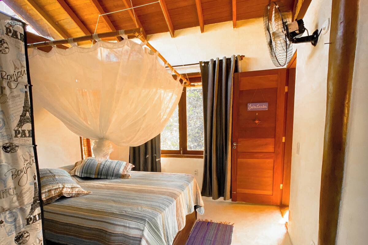 A cozy bedroom with two beds, a mosquito net, a fan, and a view of the outside.
