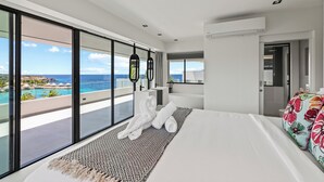 Habitación de hotel moderna con una cama grande, vista al océano y un balcón con piscina.
