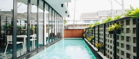 A swimming pool with glass walls, a wooden deck, and potted plants.