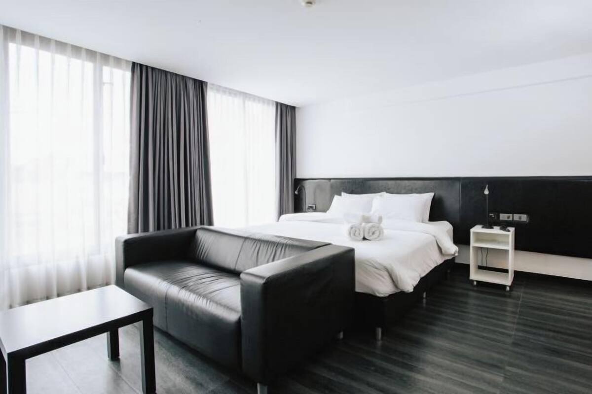Een moderne hotelkamer met een groot bed, een zwarte leren bank, een klein tafeltje en een nachtkastje.