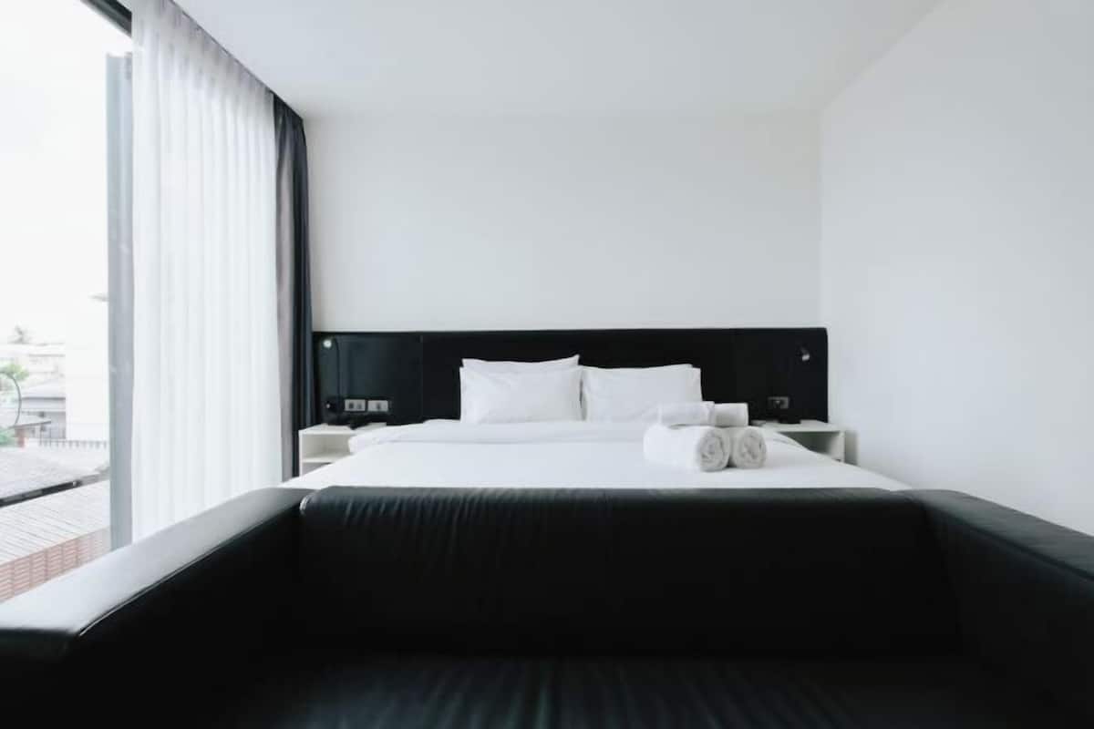 Een moderne hotelkamer met een groot bed, een zwart hoofdeinde, een raam met gordijnen en een zwarte bank.
