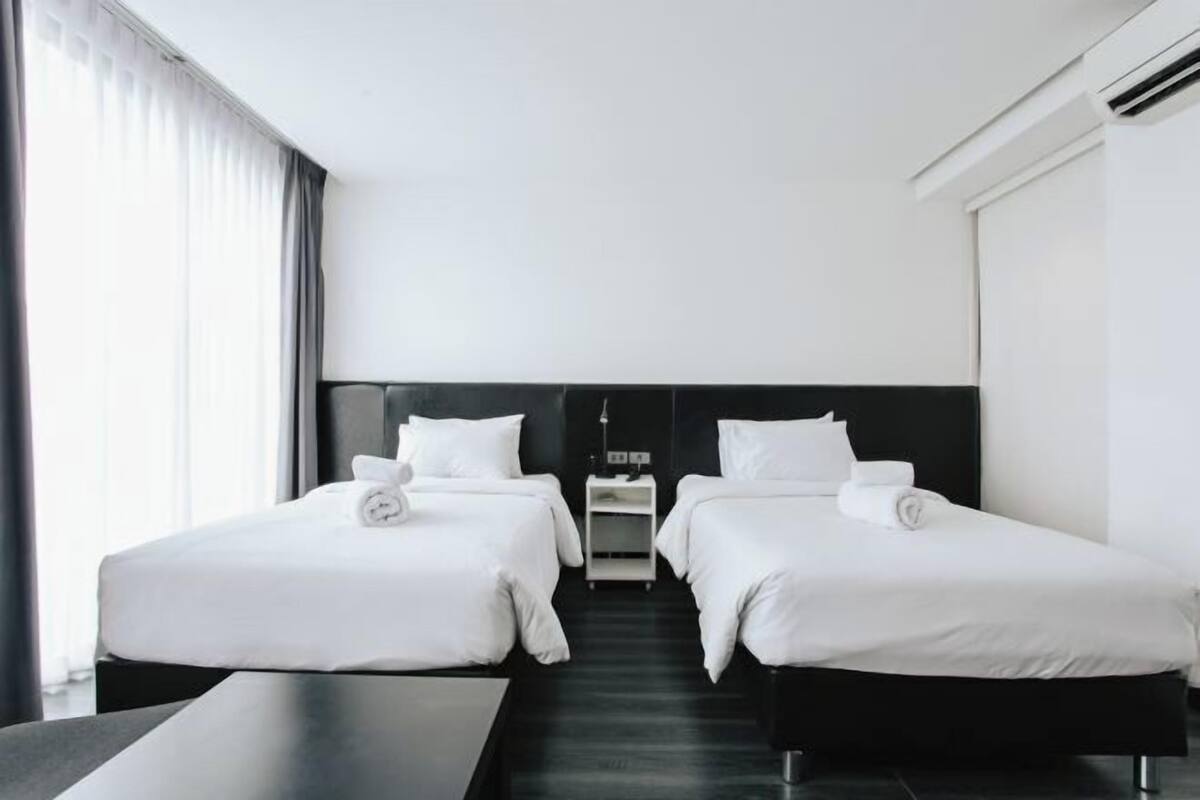 Een hotelkamer met twee bedden, nachtkastjes en een groot raam met gordijnen.