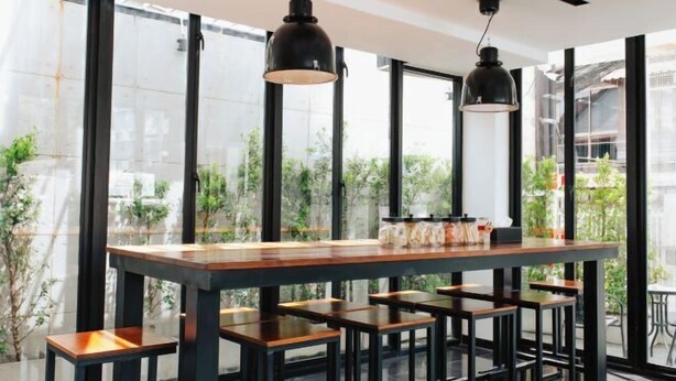 Un área de bar moderna con una mesa de madera y taburetes negros, amplias ventanas con vistas a la ciudad e iluminación colgante.