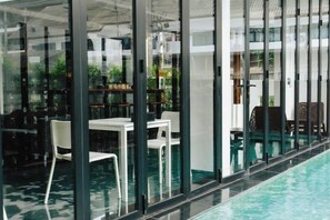 Un espace aménagé au bord de la piscine, doté de cloisons en verre, de sièges à l’intérieur et offrant une vue sur l’extérieur.