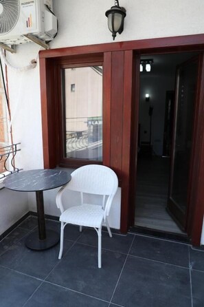 A small outdoor seating area with a round table and a white wicker chair, a wall-mounted air conditioning unit, and a door leading to an interior space. - Bruti Hotel (Prizren)