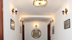 A hallway with a polished marble floor, a wooden cabinet, and wall-mounted lighting fixtures. - Bruti Hotel (Prizren)