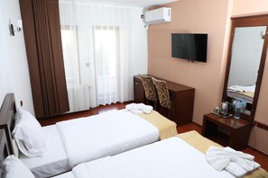 A hotel room with two beds, a TV, a desk with a chair, a mirror, and a window with curtains. - Bruti Hotel (Prizren)