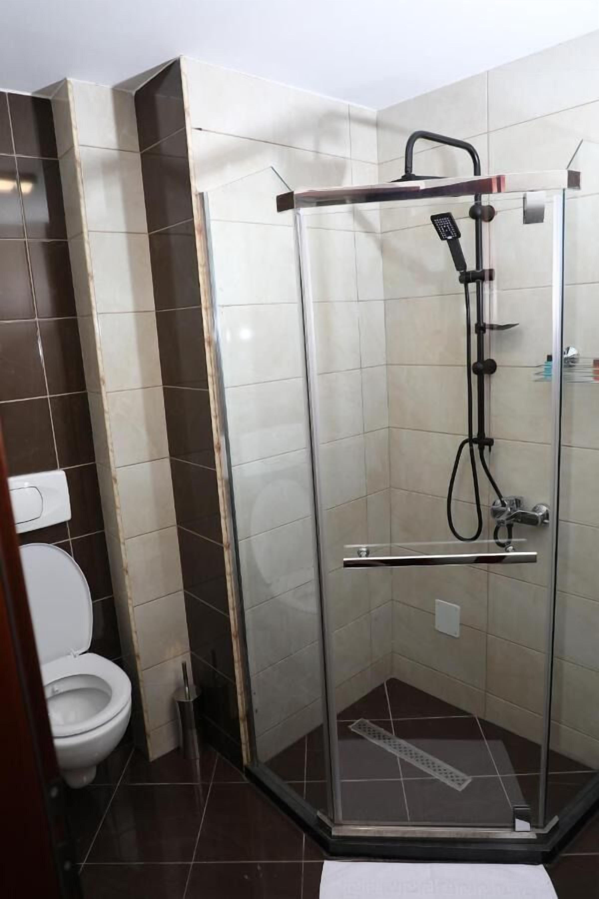 A glass-enclosed shower stall with a handheld showerhead and a handheld faucet.