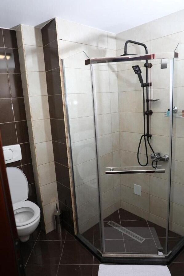 Cabina de ducha con mampara de vidrio, cabezal de ducha de mano y llave de agua de mano.
