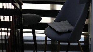 A modern room with a large window, a dark blue armchair, and a small round table. - Bruti Hotel (Prizren)