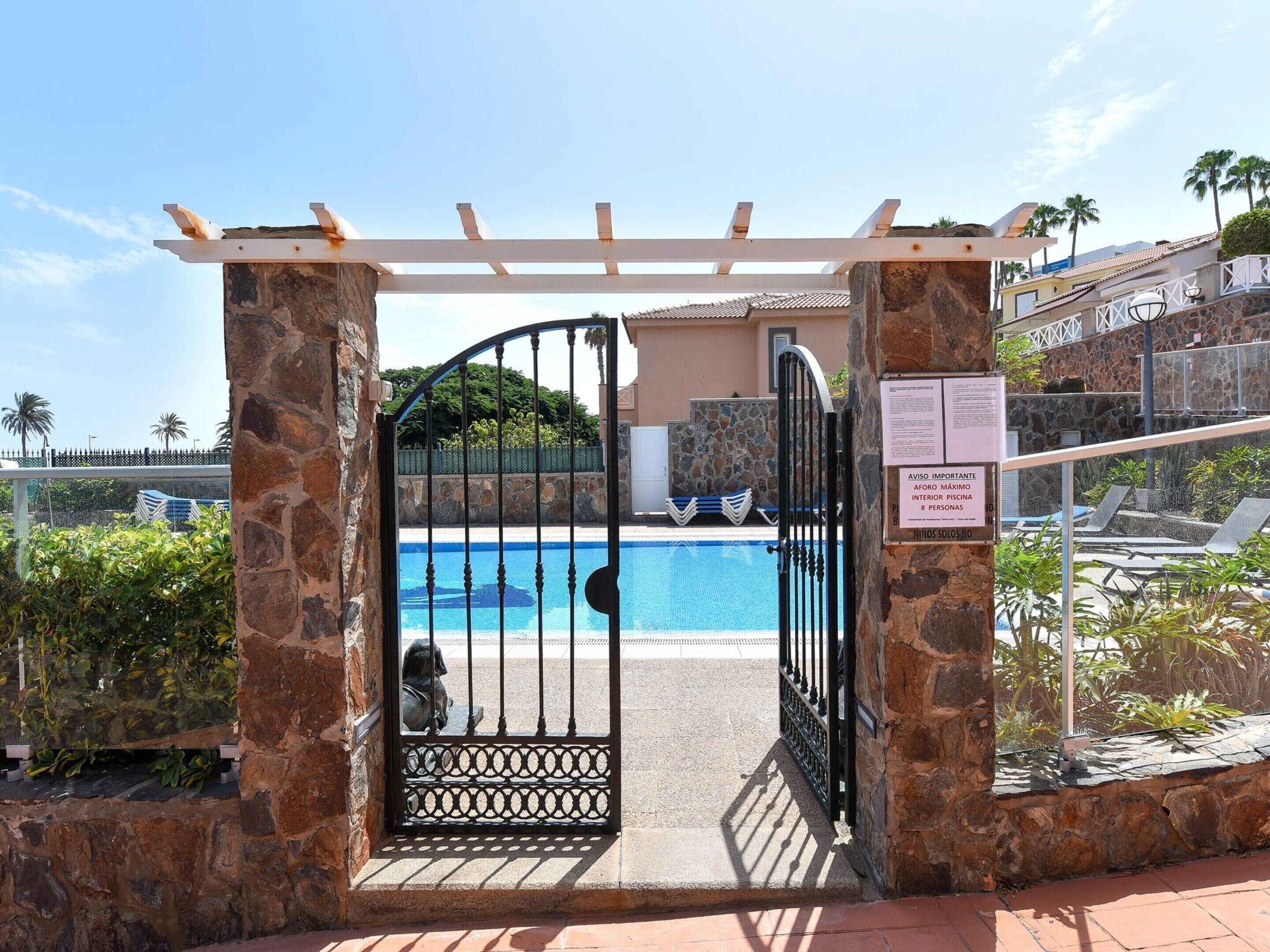 A gated entrance to a pool area with a stone wall and a pergola overhead.