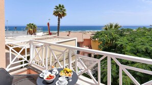 Un balcón con una mesa dispuesta para el desayuno, con vista a una playa y al océano.