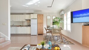 Una sala de estar moderna con una mesa de centro, un comedor con sillas, una cocina al fondo y un televisor en la pared.
