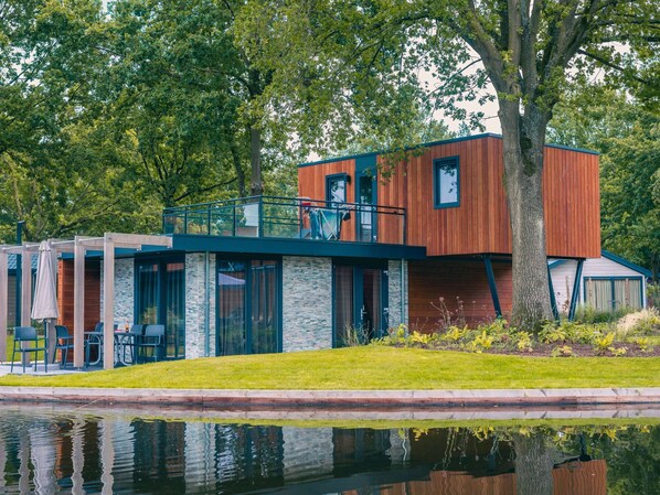Un edificio moderno con fachada de madera, un balcón y un reflejo en el agua.