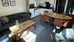 A modern living space with a sofa, coffee table, dining table, and chairs. There is a kitchen area with cabinets and appliances. - Family Getaway by Efteling (Kaatsheuvel)