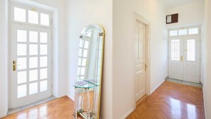 Un couloir avec des portes blanches, une table en verre avec un pied en métal et un luminaire au plafond.