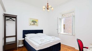 Une chambre à coucher avec un lit, un luminaire suspendu, une fenêtre et une chaise.