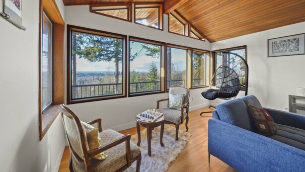 A spacious room with large windows offering a view of the outdoors, wooden ceiling beams, and a cozy seating area with a blue sofa and two chairs.