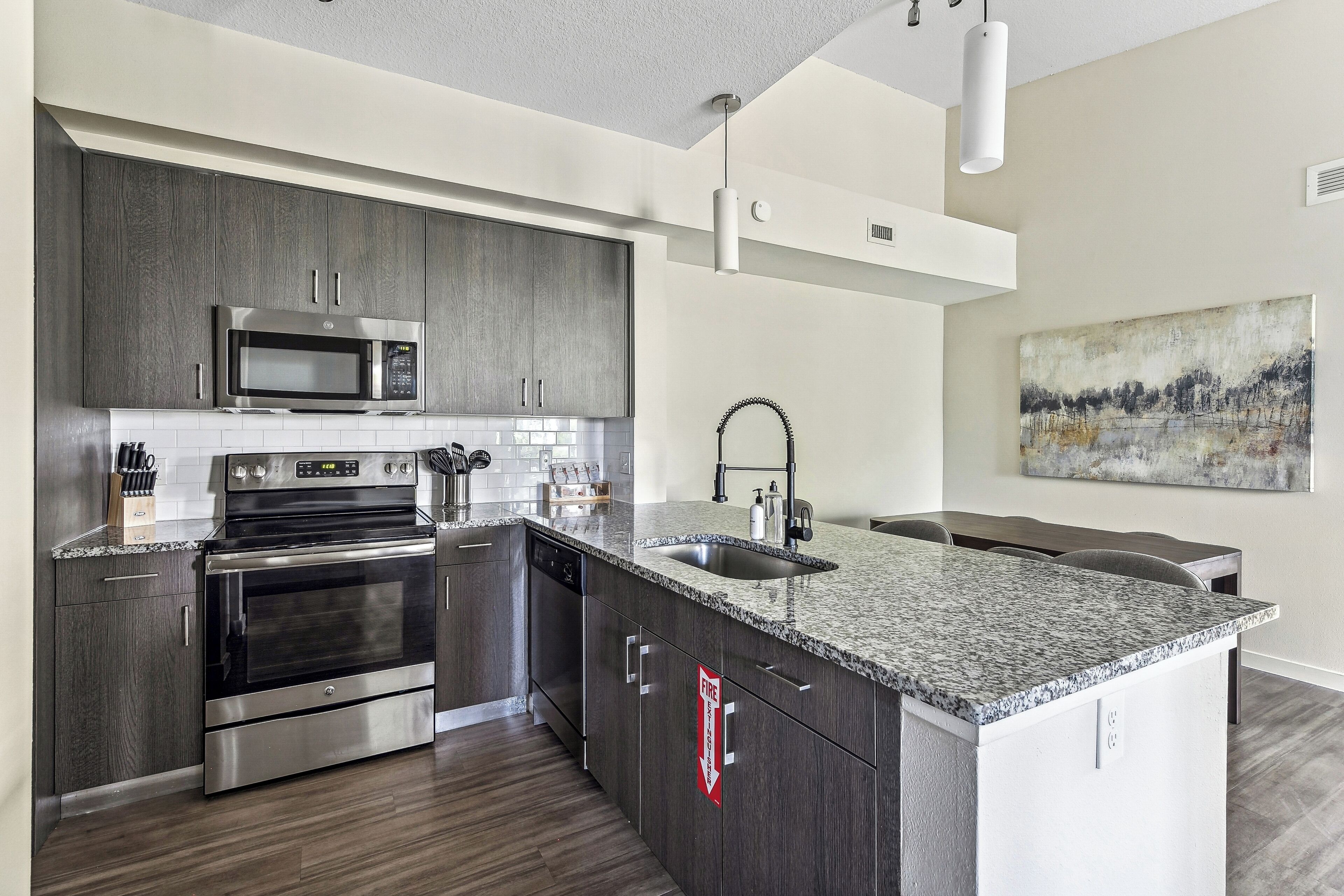 A modern kitchen with stainless steel appliances, a granite countertop, and a dining area with a view of the outdoors.
