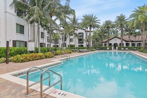 A swimming pool with a 4 ft depth marker, surrounded by palm trees and a building with multiple balconies. - Kasa Hollywood Ft. Lauderdale (Hollywood)