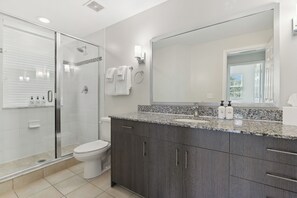 A modern bathroom with a glass shower enclosure, a toilet, and a large mirror above a granite countertop. - Kasa Hollywood Ft. Lauderdale (Hollywood)