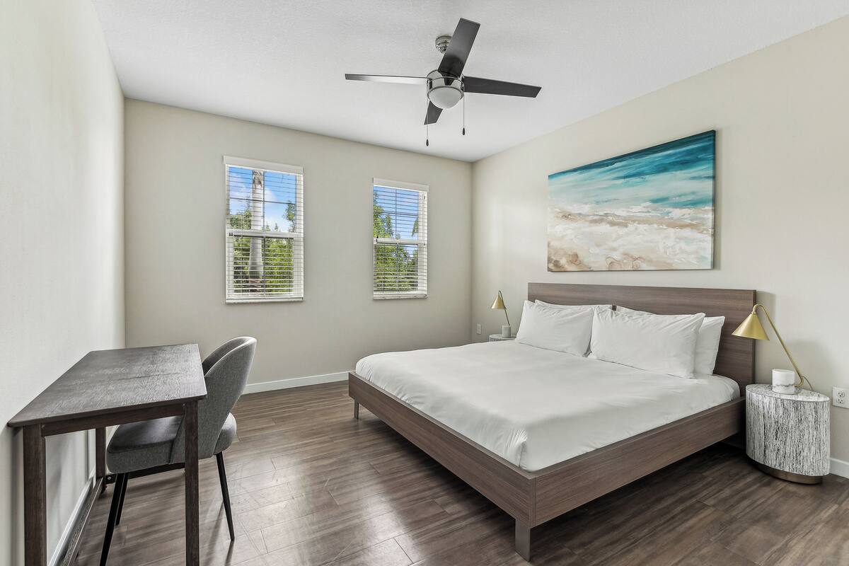 A bedroom with a bed, a desk, and two windows.