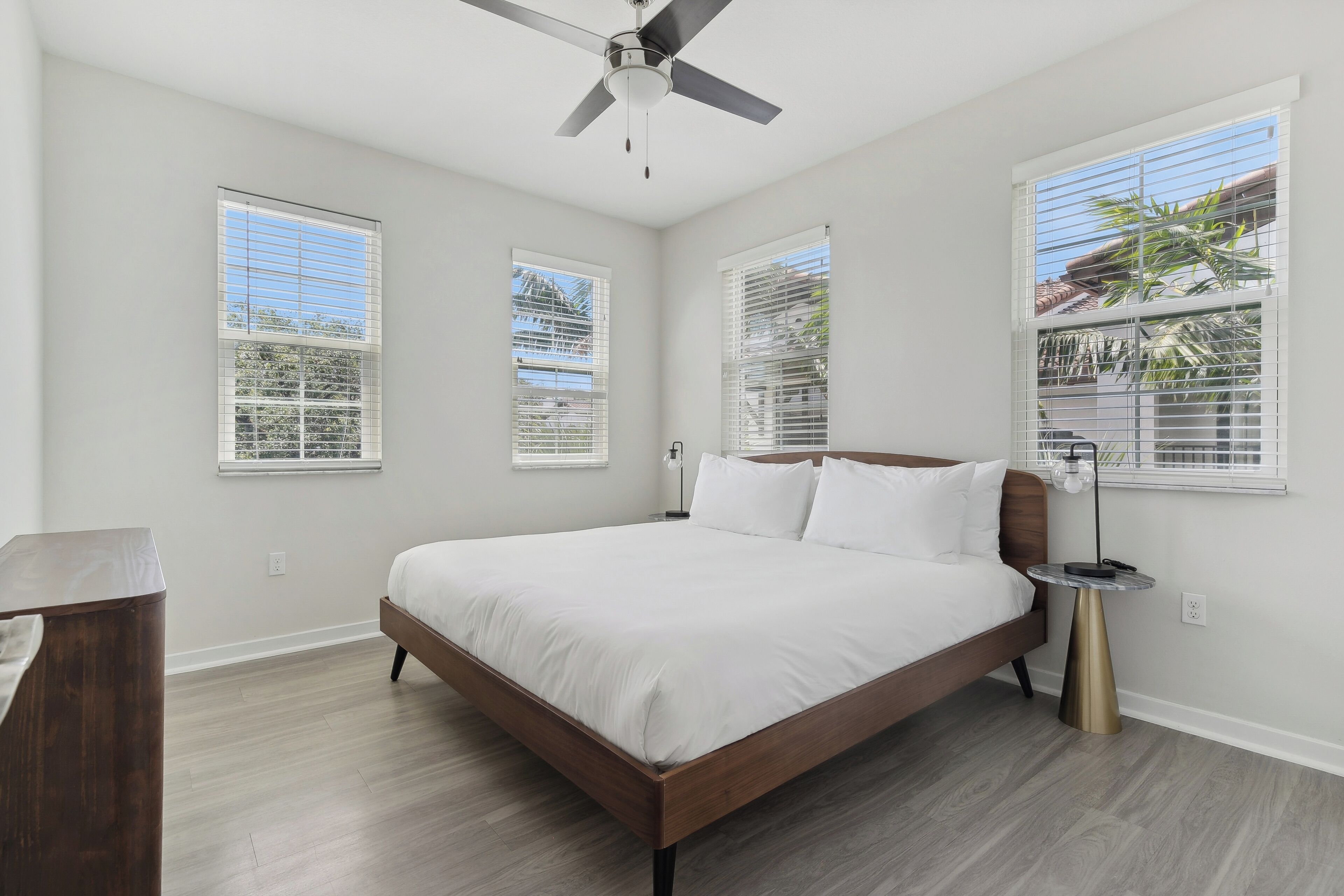 A bedroom with a bed, a ceiling fan, and large windows with blinds.