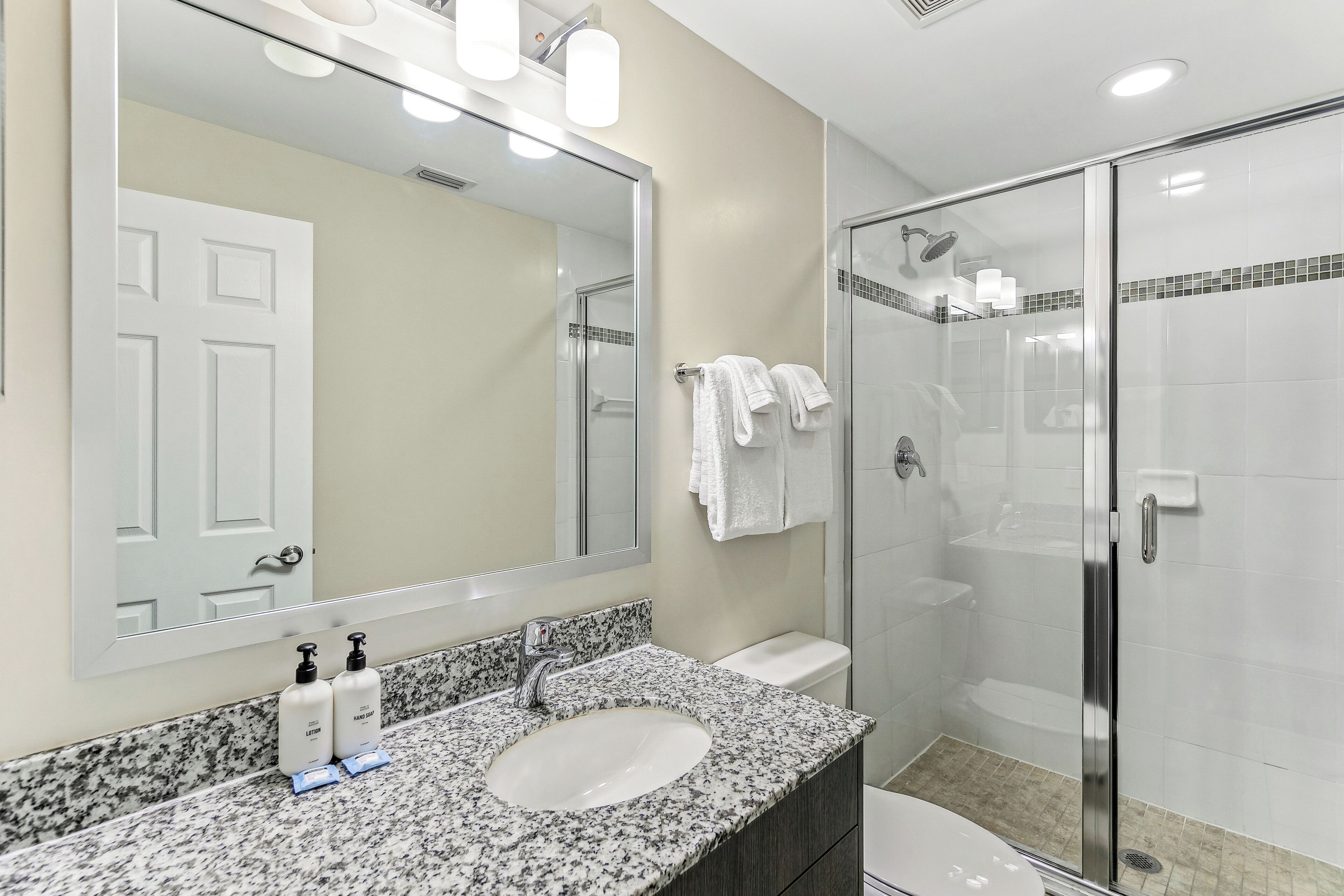 A bathroom with a granite countertop, a white sink, a large mirror, and a glass-enclosed shower area.