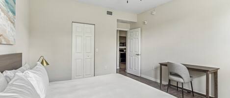 A bedroom with a bed, a desk, and a chair. There is a ceiling fan, a door, and a wall-mounted lamp.