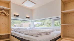 A wooden bed with a view of greenery outside, a skylight, and built-in shelves. - Cozy Lodge Near the Beach (Kamperland)