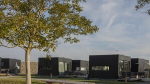 A modern outdoor area with picnic tables, a tree, and contemporary buildings. - Cozy Lodge Near the Beach (Kamperland)