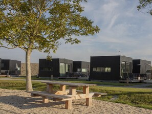 A modern outdoor area with picnic tables, a tree, and contemporary buildings. - Cozy Lodge Near the Beach (Kamperland)