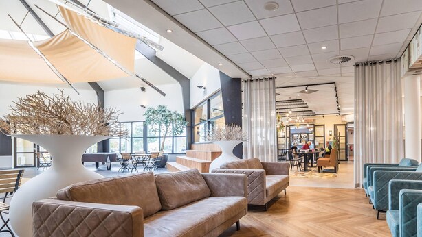 A modern interior with a wooden herringbone floor, a large white vase with branches, and a seating area with sofas and chairs. - Cozy Lodge Near the Beach (Kamperland)