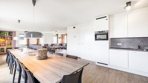 A modern kitchen with white cabinetry, a wooden dining table, and a built-in oven. - Villa in Weerterbergen With Private Sauna (Weert)