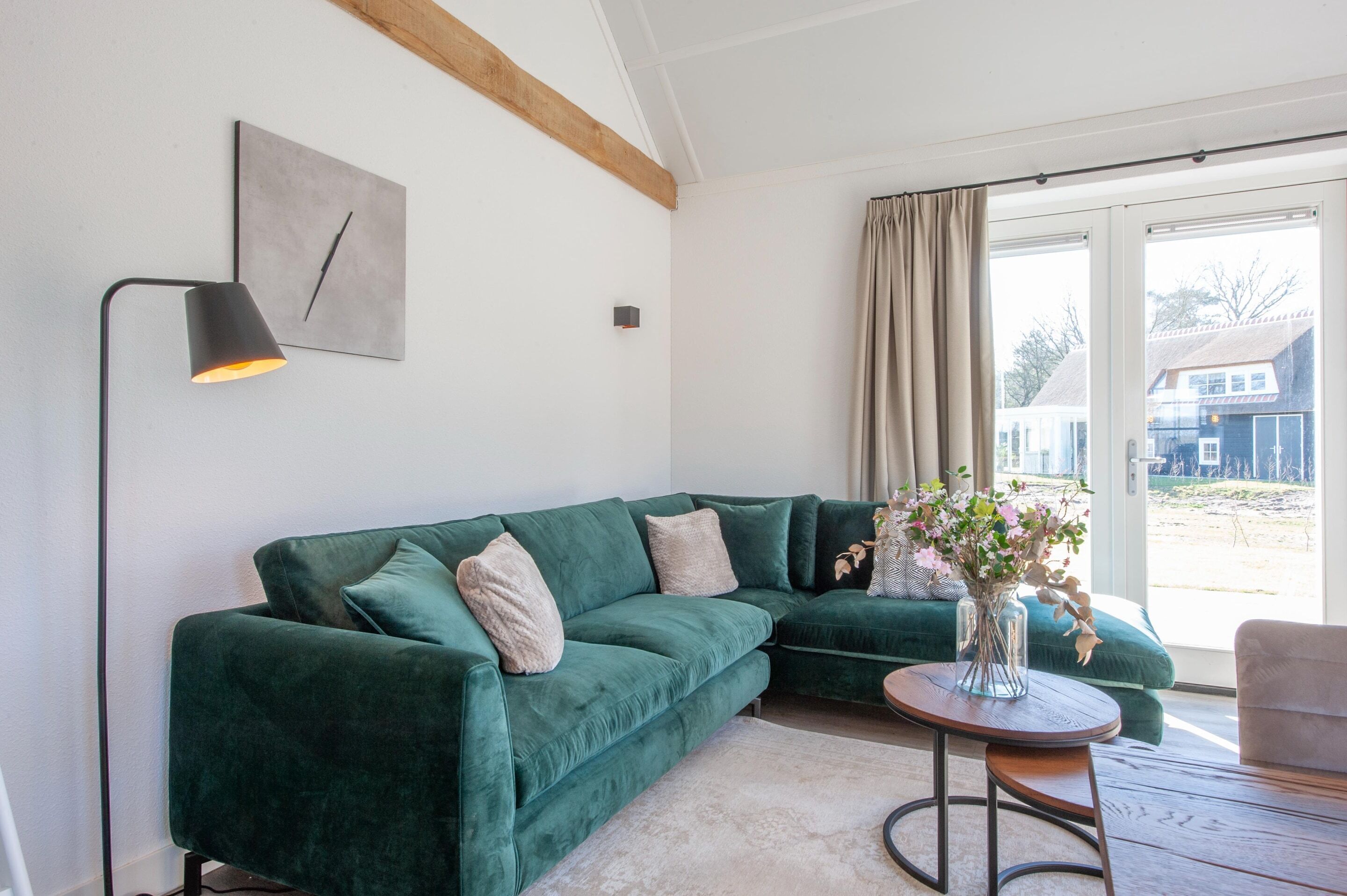 A green sofa, a small table with a vase, a floor lamp, and a window with curtains.