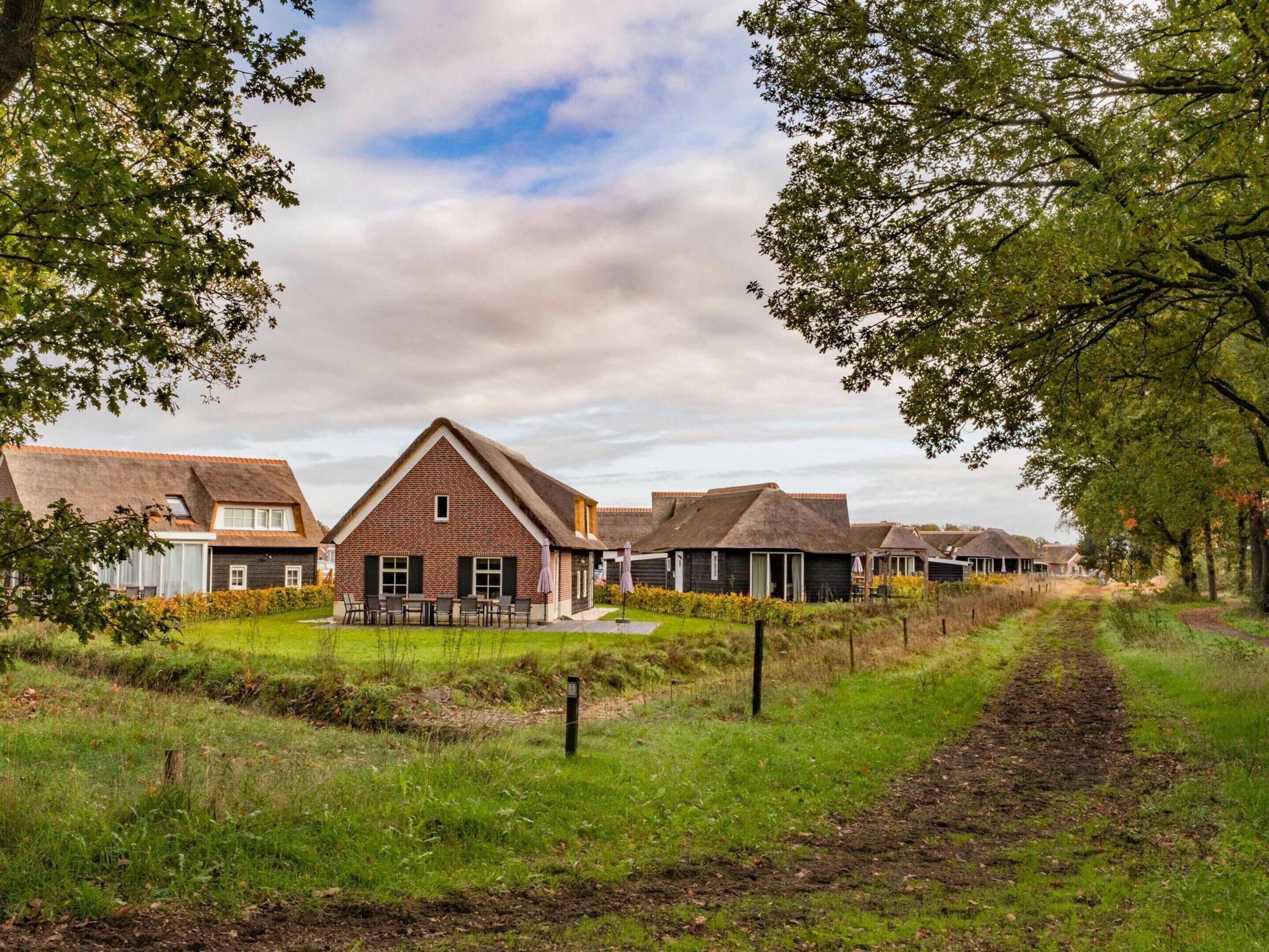 A row of traditional-style cottages with thatched roofs, surrounded by lush greenery and a clear sky.