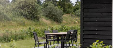 Patio esterno con tavolo e sedie, immerso nel verde e coperto da una struttura con tetto in paglia.