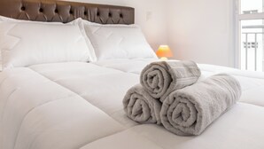 A neatly made bed with a tufted headboard, a rolled-up towel, and a bedside lamp. - Akile Bela Vista Tatro Renault (São Paulo)